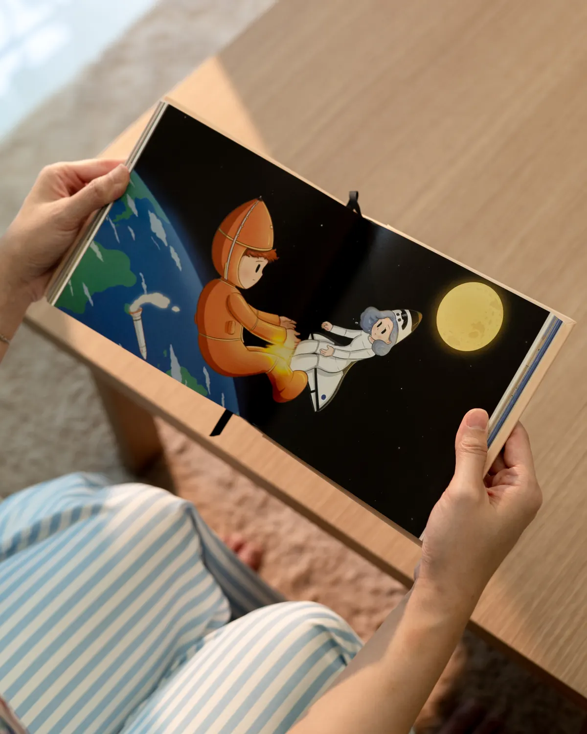 Two hands holding the book open to a spread of two astronauts floating toward the moon