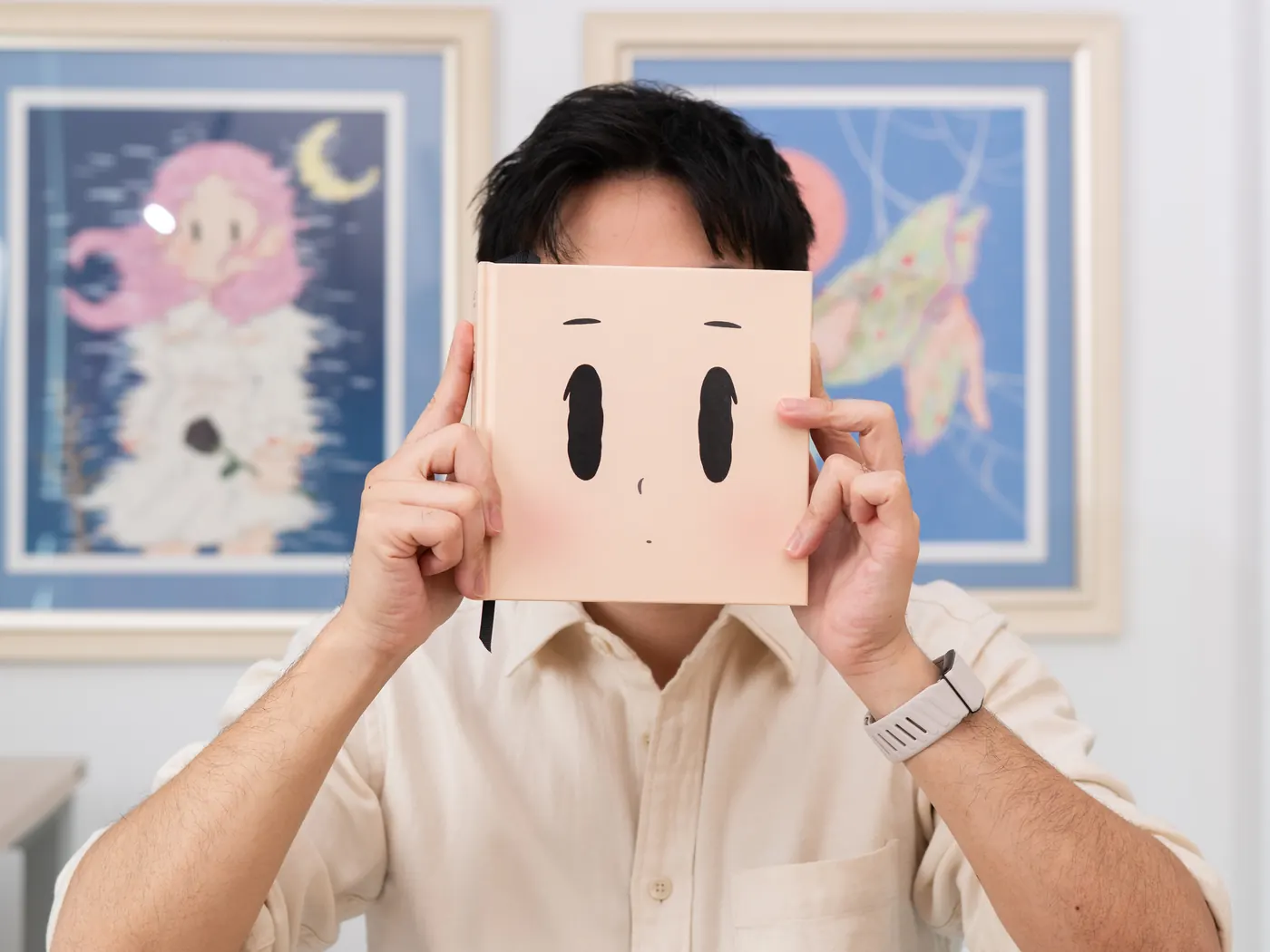 Tum Ulit holding The Art of Saying Nothing in front of his face, framed prints of his work behind him